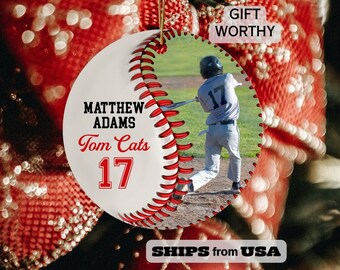 May include: White and red baseball ornament with a photo of a baseball player in a blue jersey with the number 17. The ornament has the text "Matthew Adams Tom Cats 17" printed on it.