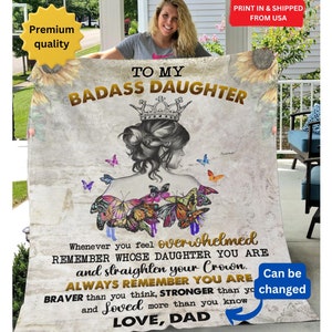 Puede incluir: Una manta de forro polar beige suave con un diseño de mariposa colorido y el texto "To My Badass Daughter" en letras doradas. El texto "Whenever you feel overwhelmed Remember whose daughter you are and straighten your crown. Always remember you are braver than you think, stronger than you and loved more than you know Love, Dad" también está impreso en la manta.