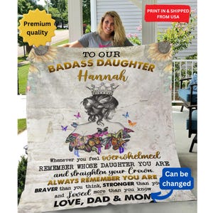 Puede incluir: Una manta de forro polar suave y blanca con un diseño dorado y negro que presenta una corona, mariposas y el texto "To Our Badass Daughter Hannah" y "Whenever you feel overwhelmed remember whose daughter you are and straighten your crown. Always remember you are braver than you think, stronger than you know and loved more than you know. Love, Dad & Mom."