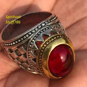 May include: A silver and gold ring with a red gemstone. The ring has a detailed design with a checkered pattern and a gold band around the gemstone.