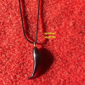 Puede incluir: Colgante negro con forma de cuerno en un collar de cordón negro. El colgante está hecho de piedra negra pulida y tiene un acento dorado en la parte superior.