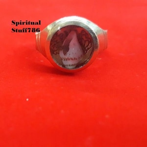 May include: A silver ring with a clear glass setting containing a small, white seashell. The ring is on a red velvet background.