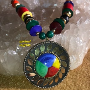 Może przedstawiać: Kolorowy naszyjnik z koralików z dużym okrągłym wisiorem, który przedstawia wielokolorowy okrągły wzór. Wisiorek jest otoczony złotą ramką z liściastymi akcentami.