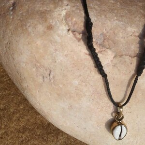 May include: A black cord necklace with a white and gold pendant. The pendant is shaped like a coffee bean.