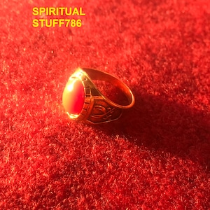 May include: A gold ring with a red gemstone and intricate details. The ring is on a red velvet surface.  "SPIRITUAL STUFF786" is written in yellow text above the ring.