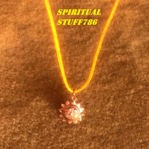 Może przedstawiać: Naszyjnik ze sznurka w kolorze żółtym z zawieszką w kształcie złotego słońca. Słońce ma twarz z trzecim okiem na czole. W obrazie widoczny jest tekst "SPIRITUAL STUFF786".