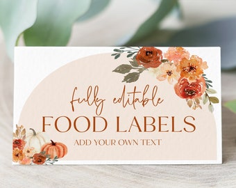 May include: A printable food label template with a fall theme. The design features a peach background with a semi-circle shape, orange and white pumpkins, and orange and yellow flowers. The text reads "fully editable FOOD LABELS ADD YOUR OWN TEXT".