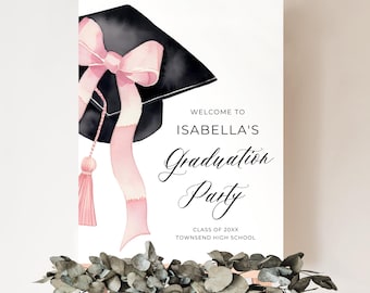 Peut inclure: Une pancarte blanche avec un chapeau de graduation noir et un ruban rose. La pancarte indique "Bienvenue à la fête de graduation d'Isabella, Classe de 20XX, Townsend High School."