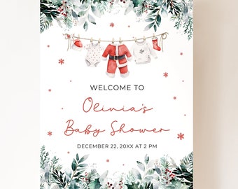 May include: A baby shower sign with a festive Christmas theme. The sign features a clothesline with baby clothes, including a Santa suit. The text reads "Welcome to Olivia's Baby Shower" with the date and time.