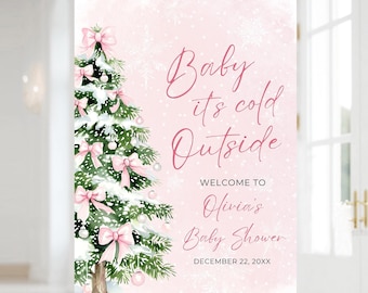 May include: A pink baby shower welcome sign with a Christmas tree illustration. The sign reads "Baby it's cold Outside" and welcomes guests to Olivia's Baby Shower on December 22, 20XX. The tree is decorated with pink bows and ornaments.