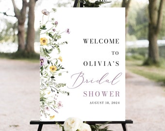 May include: A white welcome sign with a floral design in shades of purple, yellow, and green. The sign reads "Welcome to Olivia's Bridal Shower August 18, 2024".