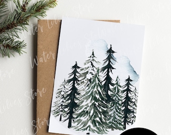 May include: A watercolor painting of a snowy forest with dark green pine trees. The painting is on a white card with a brown envelope behind it. The text "Mockup PSD Smart Object + JPG" is on a black circle.