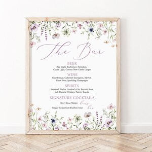 May include: A printable sign with a floral border and the text "The Bar" in a purple script font. The sign lists various beer, wine, spirits, and signature cocktails.