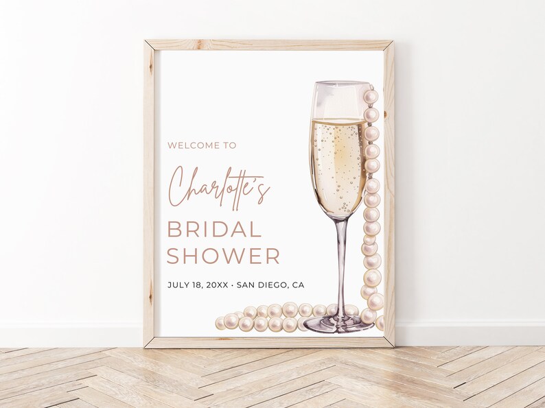 May include: A white sign with a wooden frame, featuring a champagne flute with a pearl necklace draped over it. The text reads "Welcome to Charlotte's Bridal Shower, July 18, 20XX - San Diego, CA".
