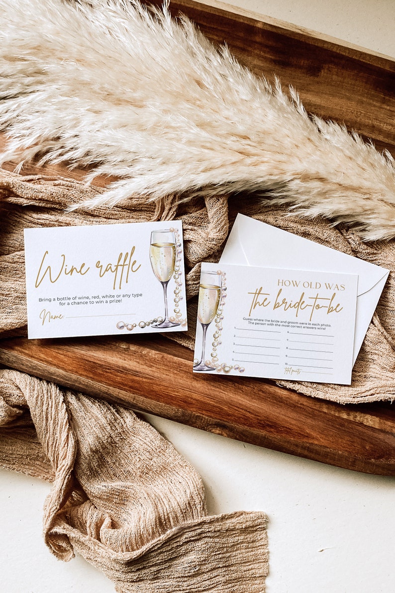 May include: Two cards for a bridal shower party. One card is a wine raffle card with a glass of champagne and pearls. The other card is a "How old was the bride-to-be" game with a glass of champagne and pearls.