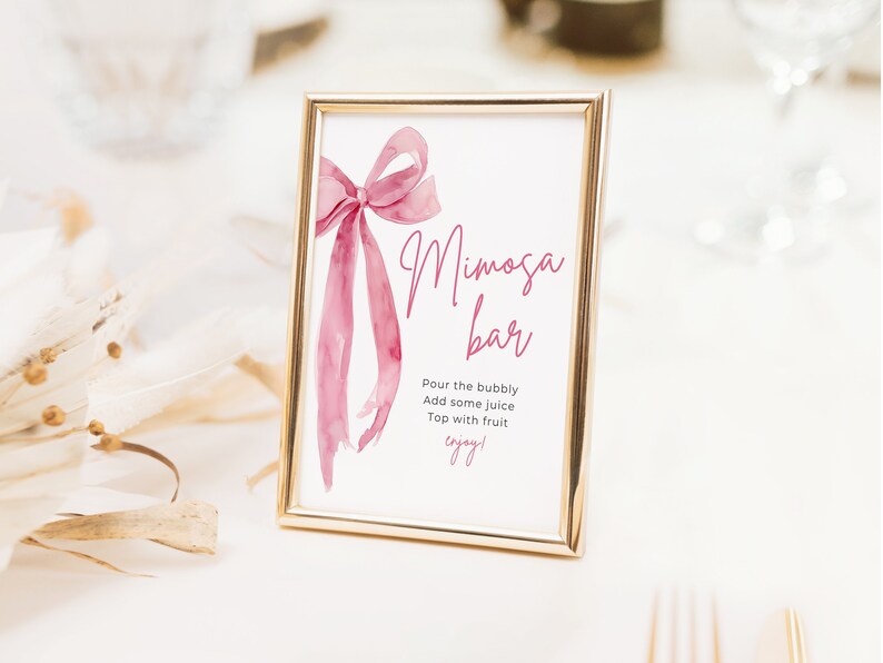 May include: A gold-framed sign with a pink watercolor bow and the text "Mimosa Bar" with instructions to "Pour the bubbly, Add some juice, Top with fruit, enjoy!"