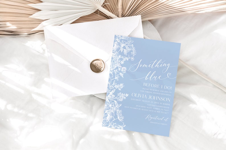 May include: A light blue invitation card with white floral designs and the text "Something Blue Before I Do!"  Olivia Johnson Saturday, August 22, 2023 at 4:00PM  Katherine's Garden, 123 Main Street  RSVP by July 15th to [phone number]  Registered at [website]