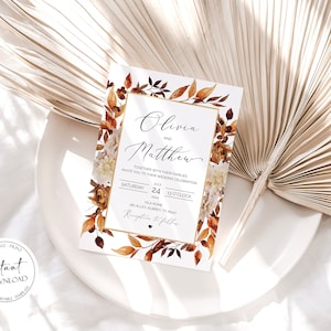 May include: A wedding invitation with a watercolor design featuring fall leaves in shades of orange, brown, and red. The invitation is for Olivia and Matthew, and it states the date and time of the wedding ceremony and reception. The text reads "Olivia and Matthew, Together with their families invite you to their wedding celebration, Saturday, July 24, 20xx, 1:00 o'clock, Villa Rome, 28 Alley Aubrey, TX 78257, Reception to follow."