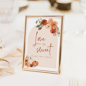 Pu&ograve; includere: Un cartello incorniciato con la scritta "Love is sweet, Please take a treat!" in un carattere decorativo. Il cartello presenta illustrazioni floreali e di zucche nei toni dell'arancione, del marrone e del verde. La cornice &egrave; dorata.