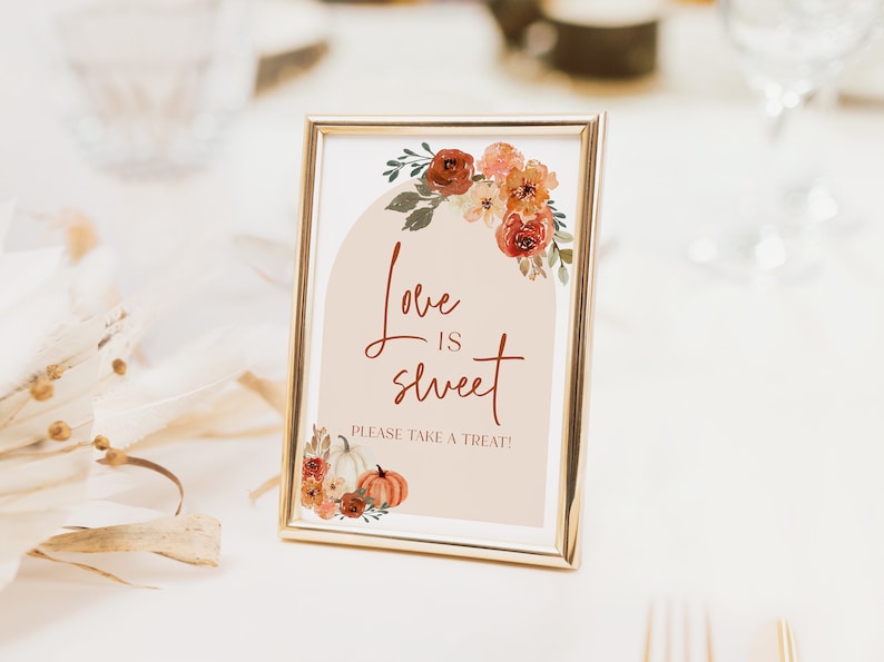 Pu&ograve; includere: Un cartello incorniciato con la scritta "Love is sweet, Please take a treat!" in un carattere decorativo. Il cartello presenta illustrazioni floreali e di zucche nei toni dell'arancione, del marrone e del verde. La cornice &egrave; dorata.