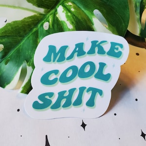 May include: A white sticker with a teal green outline and text that reads "MAKE COOL SHIT".