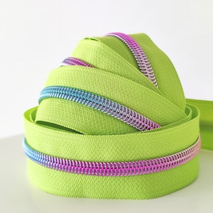 May include: Close-up of lime green zipper tape with iridescent pink and blue zipper teeth. The tape is rolled up and the teeth are visible.