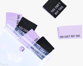 May include: A close-up of a package of woven labels with the text "You Can't Buy This" printed on them. The labels are in a variety of colors, including purple and black.
