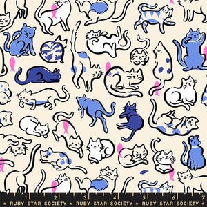 May include: A cream-colored fabric featuring a repeating pattern of cats in various poses, rendered in blue, dark blue, and black outlines, interspersed with small pink and blue fish icons. A black ruler at the bottom shows 7 inches.