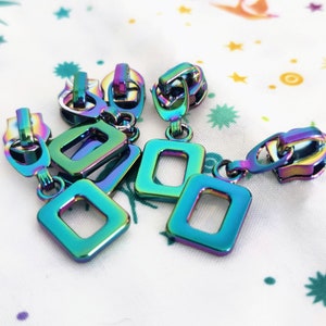 May include: Four iridescent zipper pulls with square charms. The charms are in a rainbow color scheme with blue, green, purple, and pink hues.