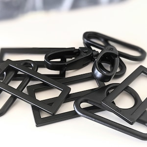 May include: A set of black metal hardware pieces, including D-rings, swivel clasps, and rectangular frames. These pieces are commonly used for crafting bags, purses, and other accessories.