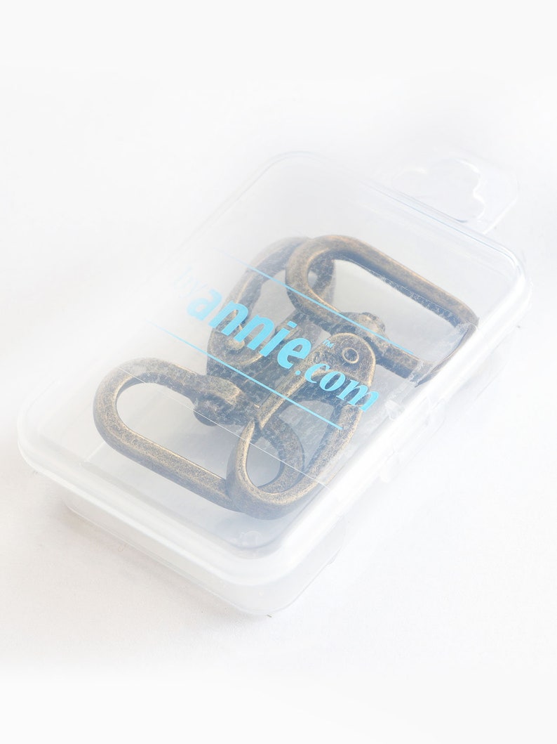 May include: A clear plastic container holding several antique bronze-colored swivel clasps. The clasps are oval-shaped and appear to be made of metal. The container has the text "annie.com" printed on it.