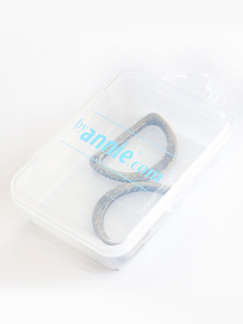 May include: A bronze-colored metal loop in a clear plastic case. The case has a blue logo that reads "byannie.com". The loop is a unique shape, possibly for a bag or craft project. The case is slightly angled.
