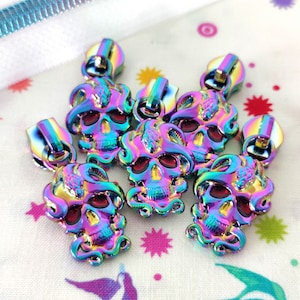 May include: Six iridescent zipper pulls with a skull design. The skulls are detailed with a snake-like pattern and have red eyes.