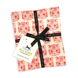 May include: A fabric fat quarter bundle featuring a repeating pattern of pink and orange cat faces on a cream background. The bundle is tied with a black ribbon printed with the text Ruby Star Society and includes a white tag labeled Oops! All Cats.
