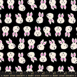 May include: Black fabric with a repeating pattern of white bunny faces and pink ears. The bunnies are stylized with a simple, cartoonish design. The fabric is from Ruby Star Society.