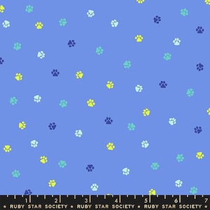 May include: A blue fabric featuring a repeating pattern of small paw prints in shades of lime green, light blue, and dark navy. A black measuring tape is visible at the bottom edge, showing measurements up to 7 inches with the text Ruby Star Society.