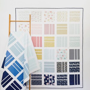May include: A large, colorful quilt with a grid pattern, featuring various fabric designs and colors, including floral prints, stripes, and solid blocks. A second quilt with a blue geometric design is draped over a wooden ladder.