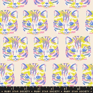 May include: A fabric print featuring a repeating pattern of cat faces in yellow, blue, and pink on a light beige background. A black measuring tape with white markings and the text RUBY STAR SOCIETY is visible along the bottom edge of the image.