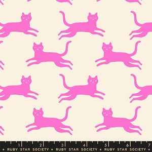 May include: A cream-colored fabric featuring a repeating pattern of bright pink cats in various poses. A black ruler at the bottom edge shows measurements in inches, with the text Ruby Star Society printed repeatedly along the black border.