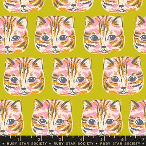 May include: A fabric pattern featuring repeating illustrations of cat faces in shades of pink, orange, and dark gray against a solid olive green background. A black measuring tape with white markings and the text Ruby Star Society is at the bottom.