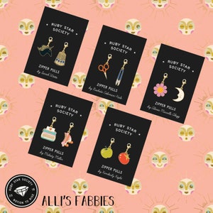 May include: Six cards with black backgrounds and gold lettering, each featuring a different zipper pull design. The cards are arranged in a grid pattern on a pink background with a repeating pattern of yellow suns. The text on the cards reads "Ruby Star Society" and "Zipper Pulls" followed by the name of the designer.