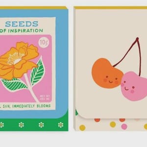 May include: Two illustrated notebooks. The left notebook features a flower design with the text "Seeds of Inspiration". The right notebook has two smiling cherries. Both notebooks have a blue, green, and yellow border.