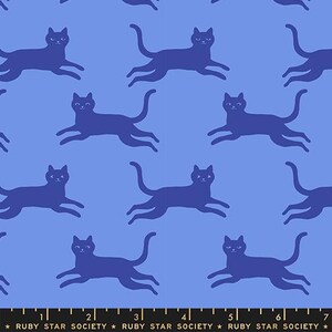 May include: A light blue fabric featuring a repeating pattern of dark blue cats in a running pose. At the bottom, a black ruler edge displays the text RUBY STAR SOCIETY with markings from 1 to 7 inches, indicating the scale of the fabric design.