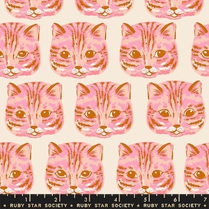 May include: A fabric pattern featuring repeating illustrations of cat faces in shades of pink and orange on a cream background. A black measuring tape with white markings and the text RUBY STAR SOCIETY is visible along the bottom edge of the image.