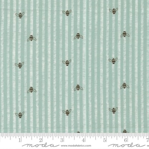 May include: A light green fabric featuring a repeating pattern of small dark brown bees and vertical white stripes. A white ruler is visible at the bottom edge, showing a measurement scale of 7 inches across the width of the textile material.