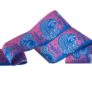 May include: Blue and pink ribbon with a repeating pattern of raccoons and squirrels. The ribbon is woven with a textured design.