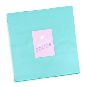 Peut inclure: Un carré de tissu turquoise clair aux bords dentelés. Au centre du tissu se trouve une étiquette rectangulaire rose clair avec une icône de diamant blanc au-dessus du texte RUBY STAR SOLIDS, le mot SOLIDS étant en lettres multicolores.