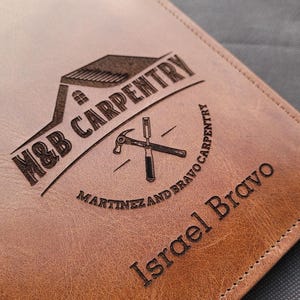 May include: Brown leather notebook with a laser engraved logo that says "M&B Carpentry Martinez and Bravo Carpentry" and the name "Israel Bravo".