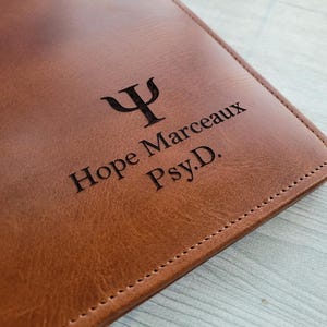 May include: A brown leather journal with the engraved text "Hope Marceaux Psy.D." and a psychology symbol.