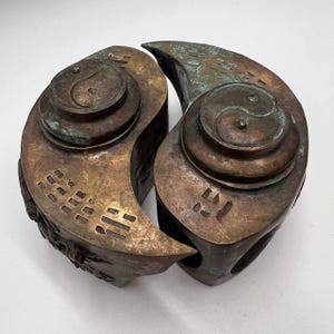 May include: Two bronze sculptures of yin yang symbols, each with a lid. The sculptures are joined together, forming a circle. The sculptures are decorated with intricate details and have a greenish patina.